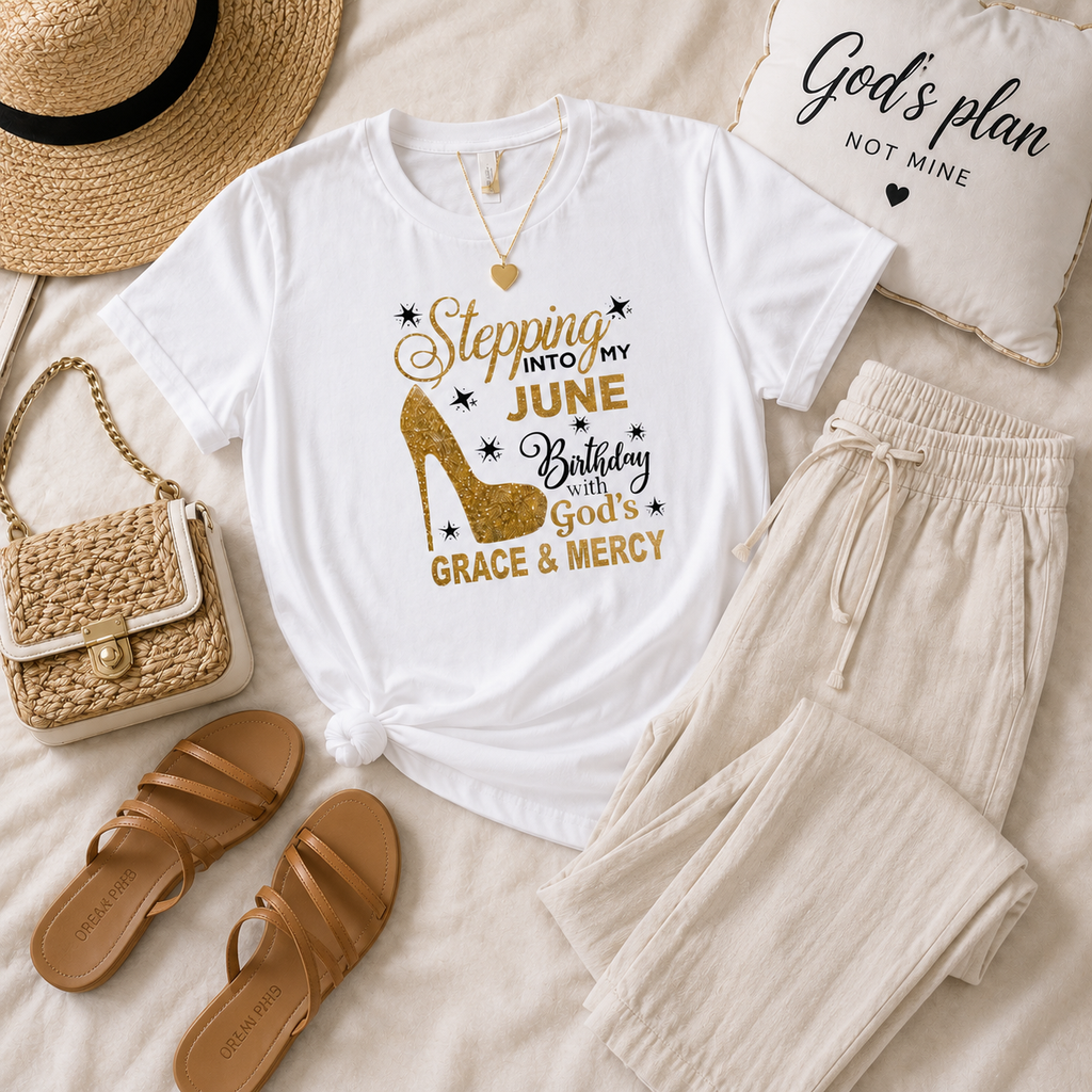 White t-shirt with high-heeled shoe graphic and text, paired with beige pants, sandals, and a straw bag on a light surface.
